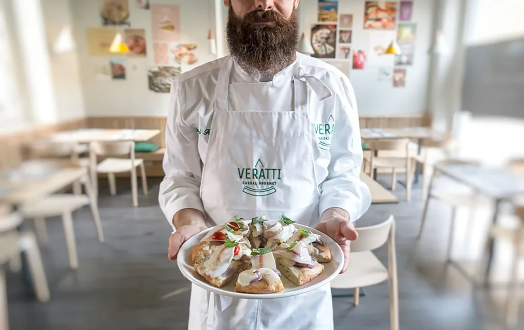 Chef di Veratti Casual Gourmet che presenta una pizza gourmet su piatto bianco.